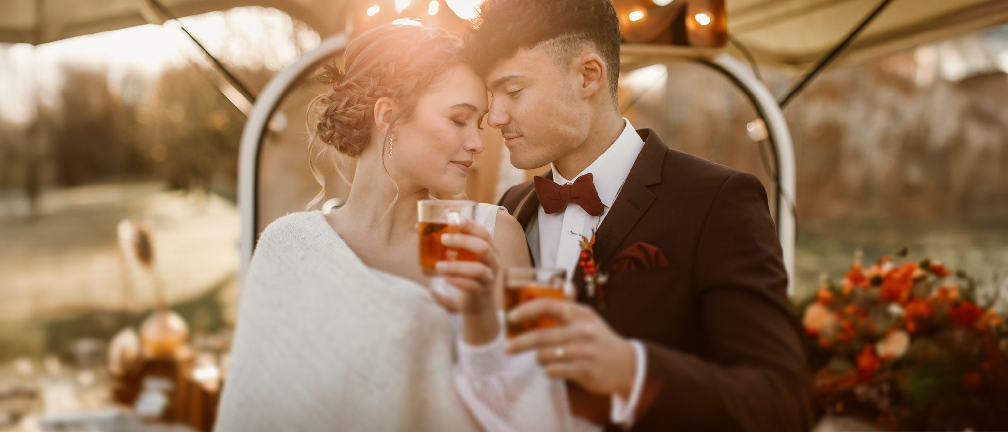 Winter-Hochzeit: Bräutigam in braunem Anzug mit bordeauxroter Fliege & Einstecktuch neben Braut in weißem Wollpullover.